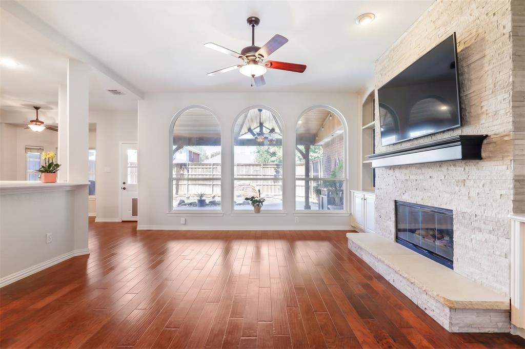 Living area featuring wood-finish flooring, a floor-to-ceiling stone-faced fireplace with a stone hearth, built-in shelving, and triple arched windows
