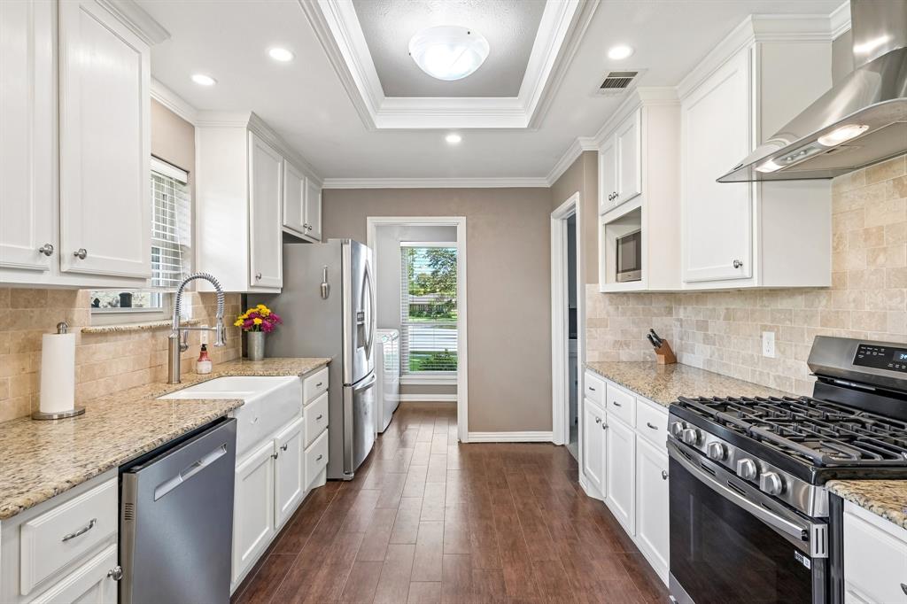 Kitchen featuring white cabinetry, granite countertops, stainless steel appliances, a farmhouse sink, and wood-finish flooring