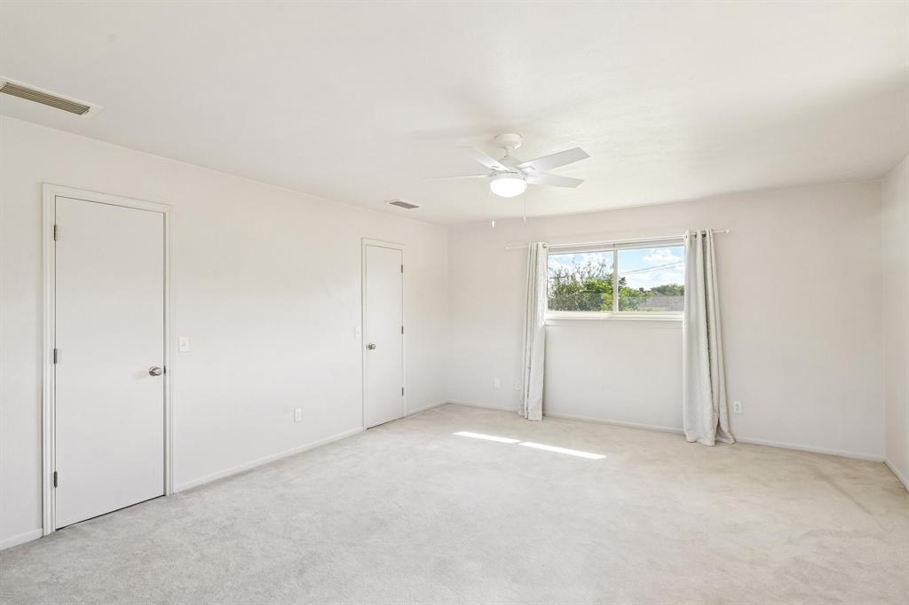 Expansive room with neutral carpeting, white walls, a ceiling fan with integrated lighting, and multiple doors