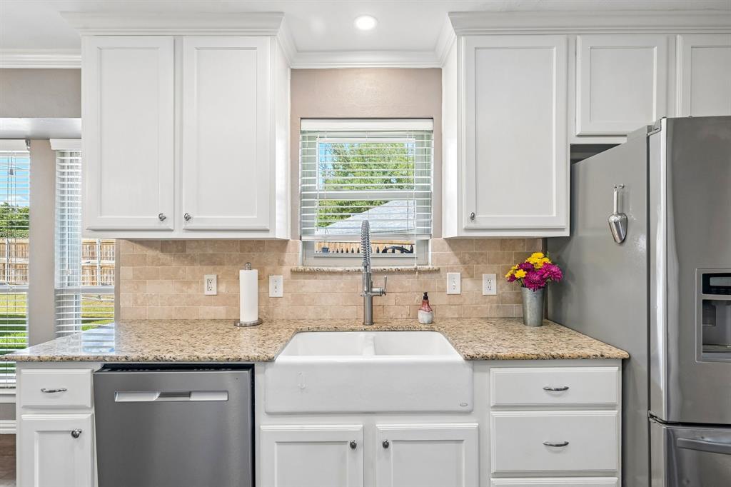 White shaker-style cabinetry with crown molding, light-toned granite countertops, a farmhouse-style sink, and a tiled backsplash