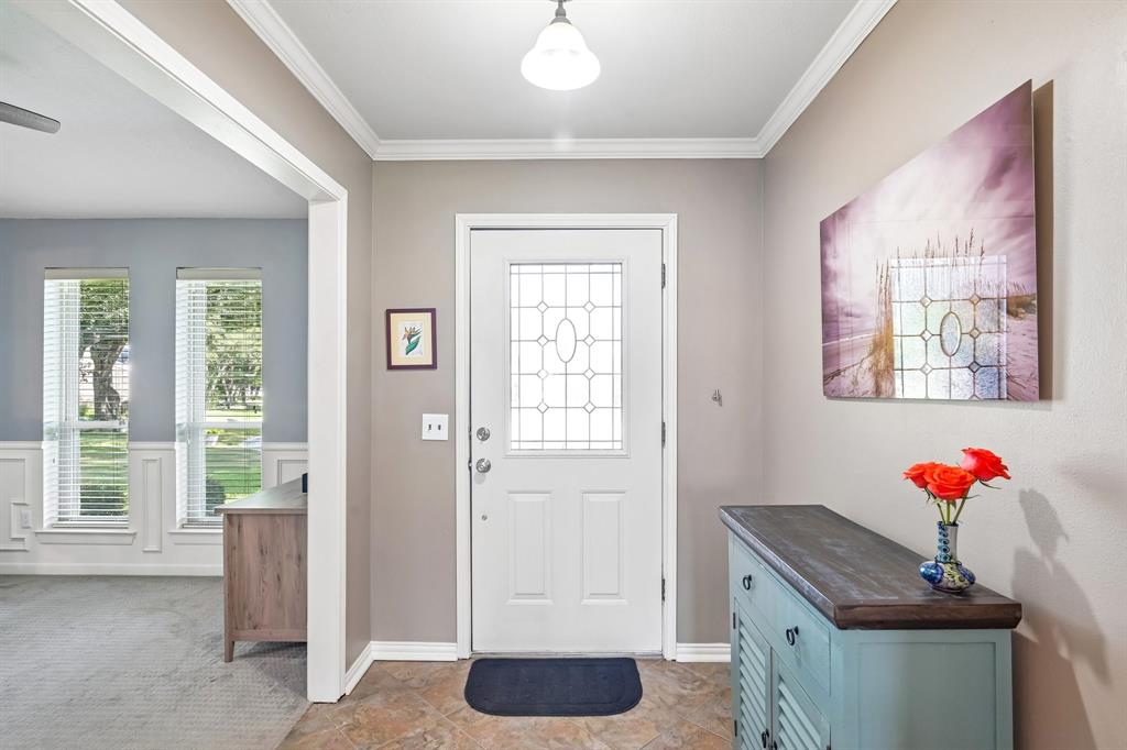 Entryway featuring decorative glass paneled front door, crown molding, and tiled flooring