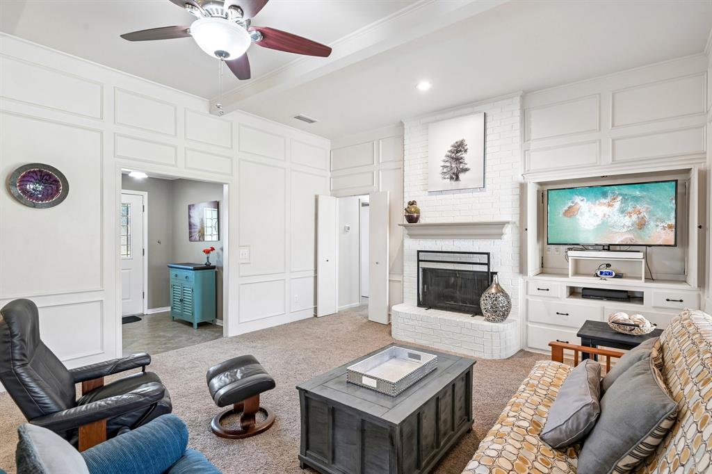 White paneled walls, ceiling fan with light fixture, brick fireplace with mantel, built-in entertainment center, and carpeted flooring