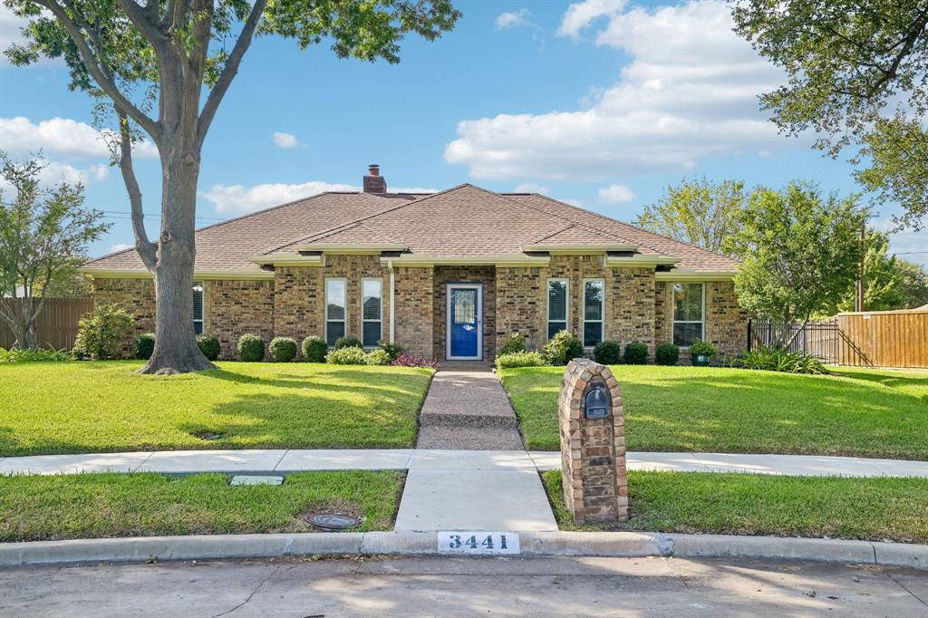 Brick facade with a contrasting blue front door, mature trees, and a stone-clad mailbox