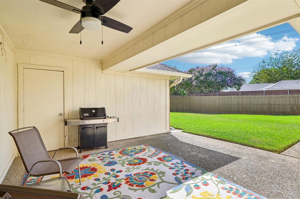 Covered patio with a ceiling fan, textured concrete flooring, and a spacious green lawn