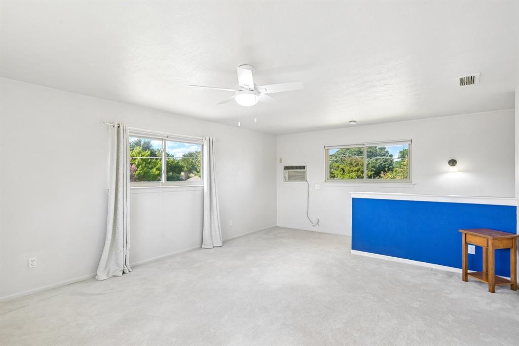 Expansive room featuring light-toned carpeting, multiple windows, a ceiling fan with integrated lighting, and a wall-mounted sconce
