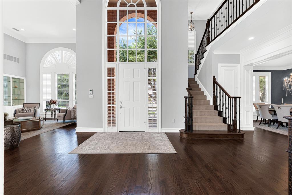 Rich hardwood floors and towering, double-height ceilings create a striking first impression as natural light floods the foyer through a dramatic arched window above the front door. It’s an inviting entrance that immediately sets an warm, sophisticated tone for greeting friends and family.