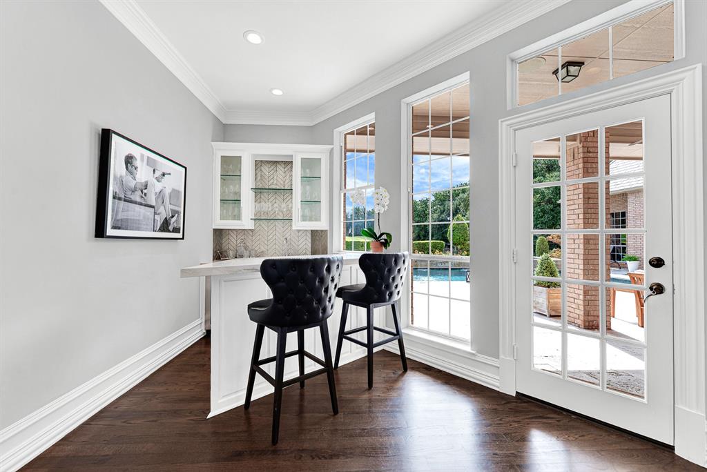 Tucked conveniently near the patio exit, this dedicated wet bar featuring counter seating serves as an ideal beverage station for indoor and outdoor gatherings. Large windows showcase pool views while French doors offer direct access to the covered entertaining deck