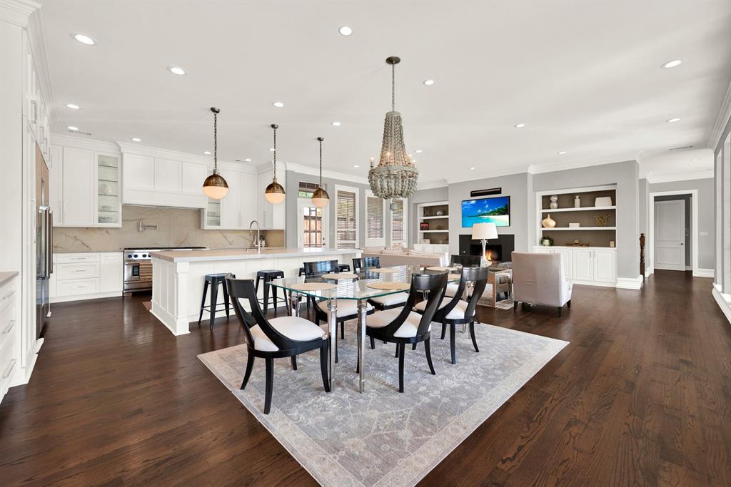 Rich hardwood floors anchor a massive, light-filled open layout that seamlessly connects the chef's kitchen, casual dining space, and main family room. Warm brass pendants and a beaded chandelier bring modern elegance to this functional hub designed for everyday family gathering