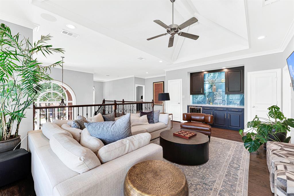Designed for host convenience, the upper game room features a wet bar alcove complete with custom blue cabinetry, a beverage fridge, and a statement tile backsplash. Open iron-spindled railings maintain an airy connection to the grand entryway below