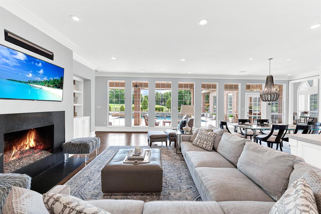 Expansive floor-to-ceiling windows line the back wall, seamlessly connecting the cozy indoor seating area with the resort-style pool deck outside. The open-concept design flows effortlessly past the modern fireplace directly into the casual dining space and kitchen.