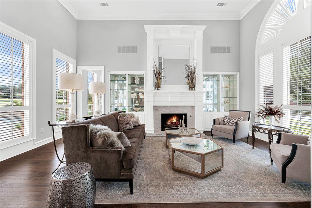 A refined white fireplace mantel flanked by lighted glass display shelves serves as the centerpiece of this comfortable, bright sitting area. Picture cozy evenings unwinding by the fire while enjoying peaceful views of the landscaped yard through plantation shutters.