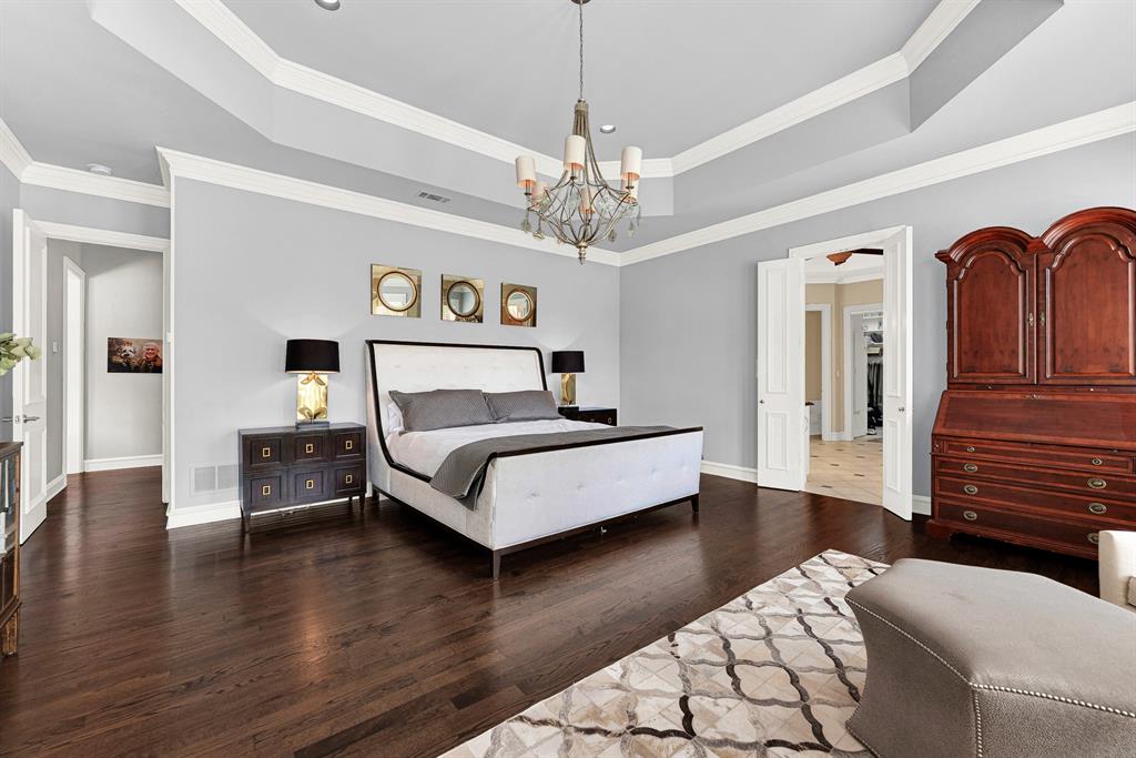 Generous square footage comfortably allows for a king-size bed setup alongside large accent dressers and custom armoires. Soft blue-gray walls, crisp white trim, and double doors opening into the ensuite bath complete this peaceful sanctuary.