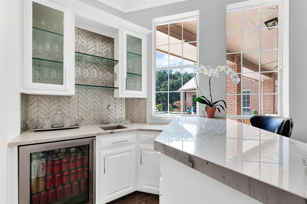 A stylish herringbone tile backsplash, quartz counters, glass-front upper cabinets, and a built-in beverage fridge make host prep effortless. Complete with a prep sink and stemware display, this wet bar delivers both high functionality and modern luxury.