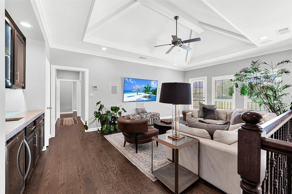 Anchored by a tray ceiling with an accent fan, this spacious upstairs lounge features a built-in wet bar with dark cabinetry along one wall. Large windows and a glass door open directly to a private balcony overlooking the pool and golf course.