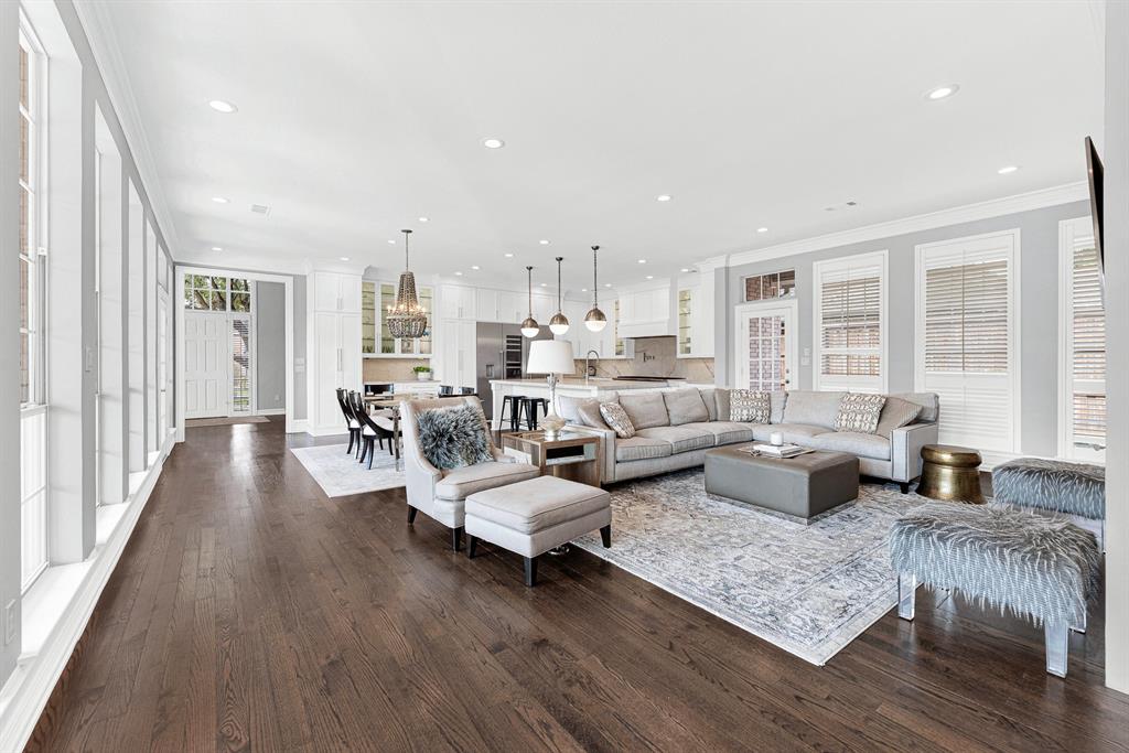 Rich hardwood floors stretch across this expansive main living area, highlighting the seamless layout connecting the family room, breakfast nook, and kitchen. Recessed lighting and floor-to-ceiling windows brighten every corner, creating an airy atmosphere built for large-scale entertaining.