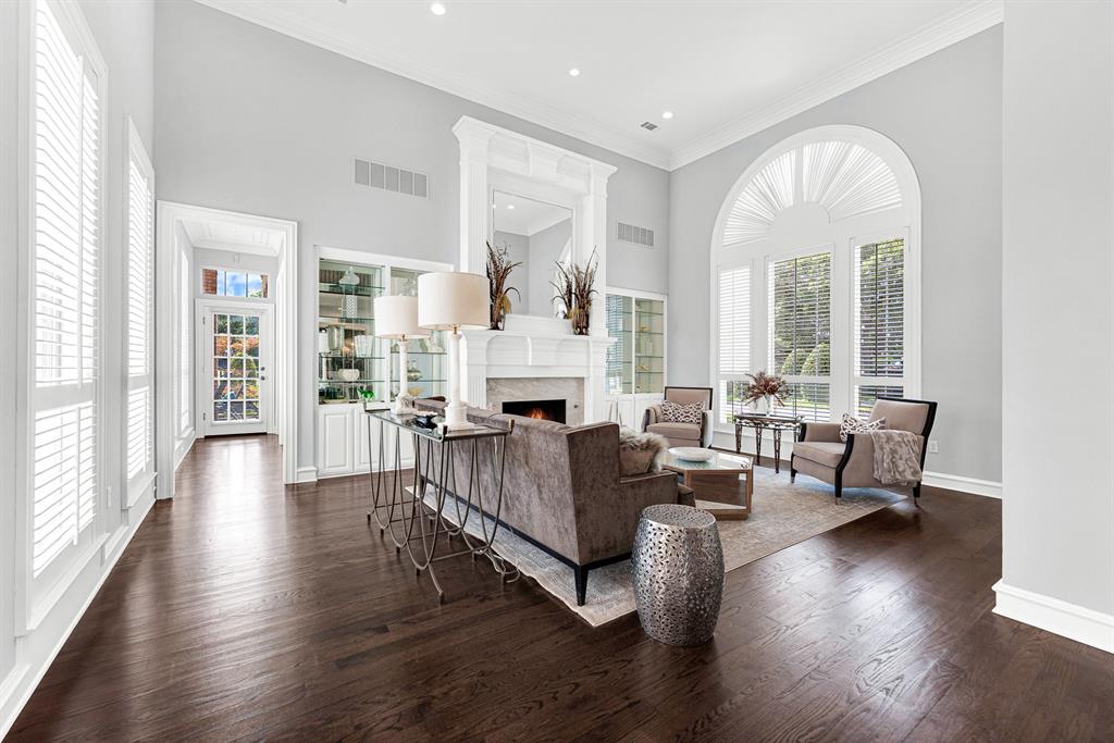 Soaring ceilings and an elegant fireplace mantle anchor this sunlit formal living space, framed by expansive arched windows and custom built-in display cabinetry. Perfect for entertaining guests, the effortless floor plan naturally flows right into the surrounding main-level living areas.