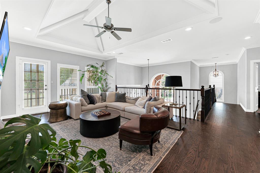 A plush sectional and leather armchair anchor this open upstairs entertainment space overlooking the main staircase landing. Large windows frame elevated backyard views, while French door access leads seamlessly out to the covered balcony.