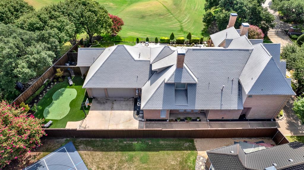 An elevated top-down view shows the home's multi-tiered slate roofline alongside the garage motor court. You can practice your game on the custom turf putting green sits tucked in the side yard, complemented by landscaping and privacy fencing.