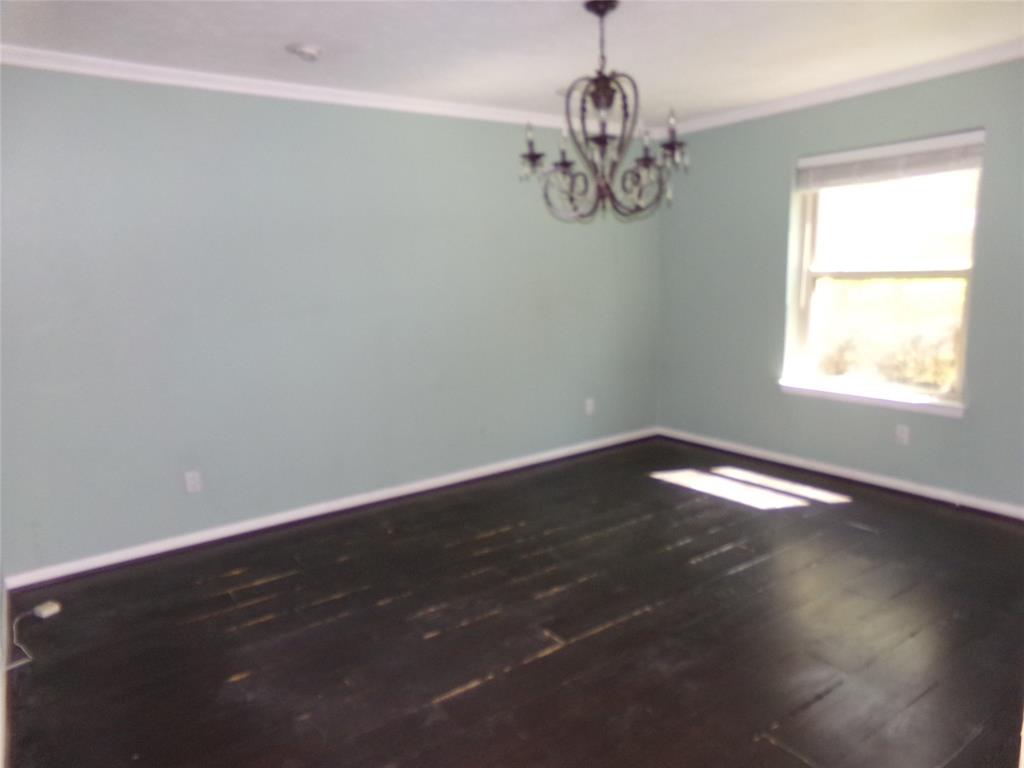 Crown molding accents a room with a single window and dark wood-finish flooring, complemented by a decorative chandelier