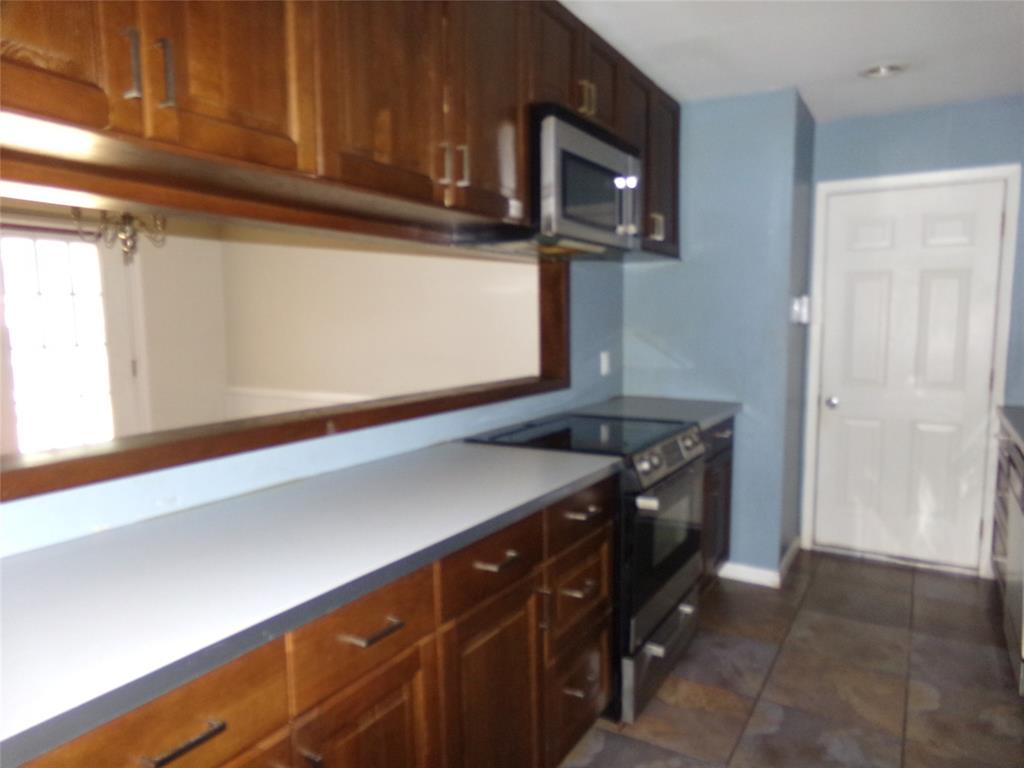 Wood-finish cabinetry with modern hardware, integrated stainless steel microwave, black electric range, and stone tile flooring