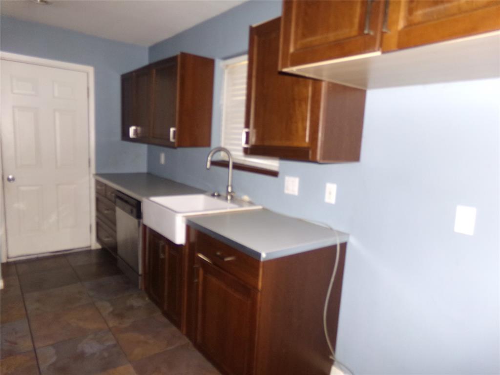Rich wood cabinetry, an apron-front sink, stainless steel dishwasher, and tiled flooring Rich wood cabinetry, an apron-front sink, stainless steel dishwasher, and tiled flooring