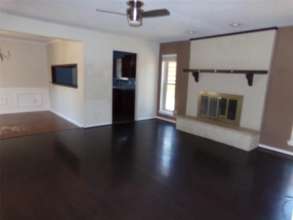 Dark wood-finish flooring, white brick fireplace with a hearth, pass-through window, and a ceiling fan Dark wood-finish flooring, white brick fireplace with a hearth, pass-through window, and a ceiling fan