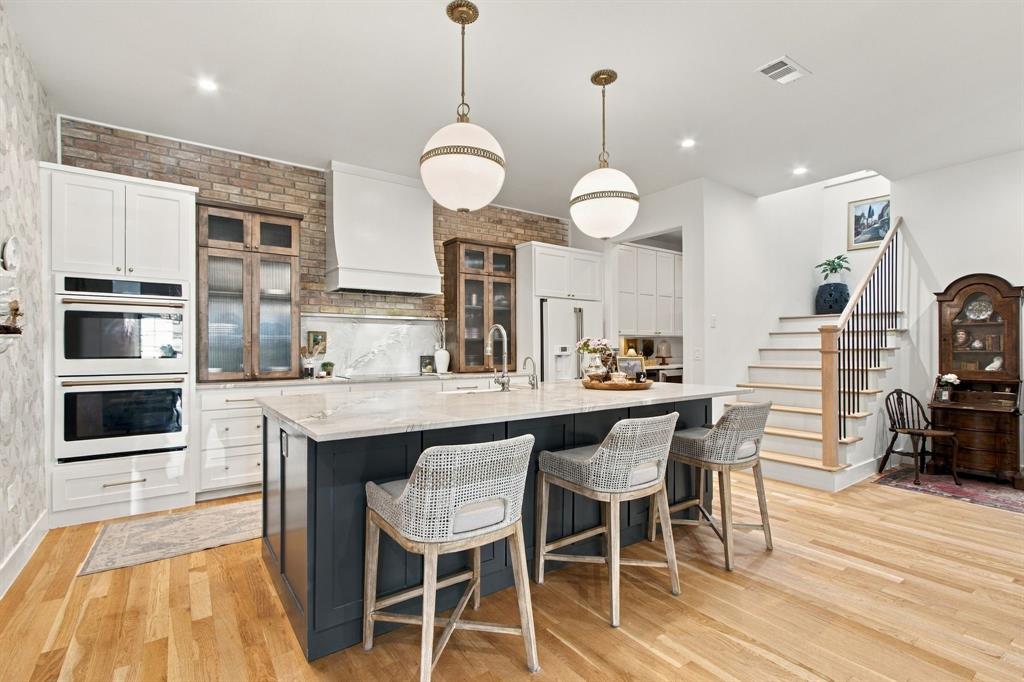 Kitchen featuring a central island with countertop seating, integrated double ovens, brick accent wall, and light wood-finish flooring