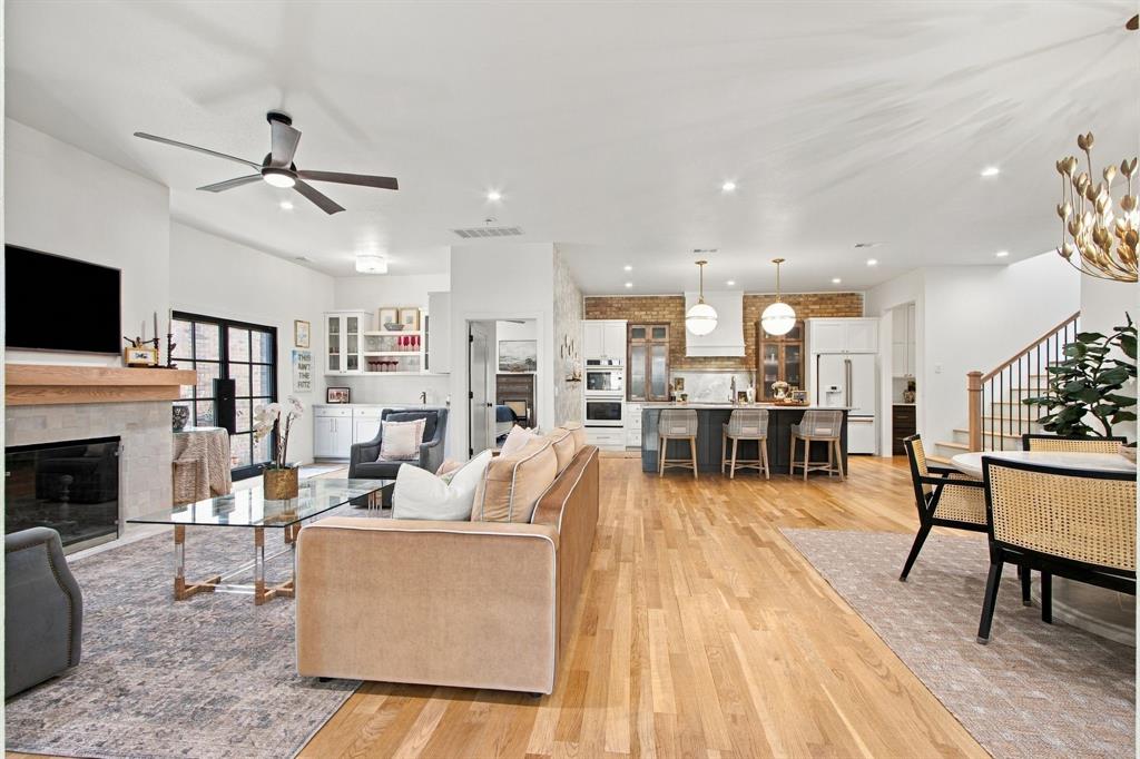 Hardwood flooring throughout, a modern fireplace with a wood mantel, a kitchen island with pendant lighting, a built-in dry bar with upper glass cabinetry, and a staircase with wood newel posts and railings
