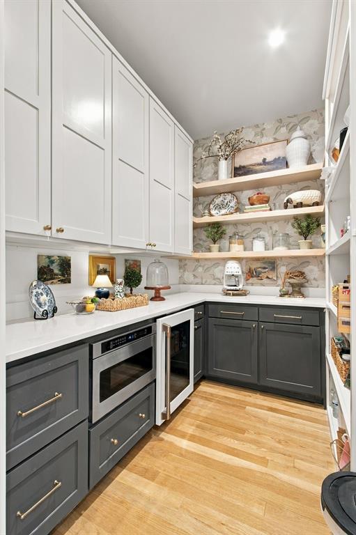 Built-in microwave, undercounter beverage cooler, wood-finish flooring, white upper cabinetry, and contrasting gray lower cabinetry