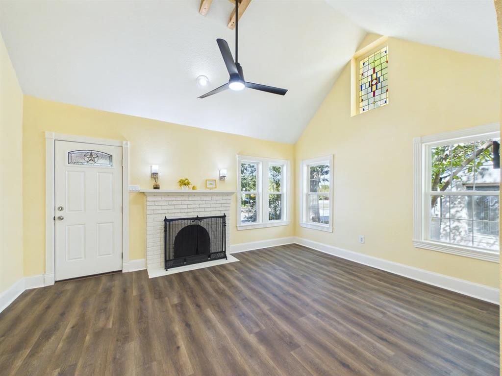 Spacious interior featuring a vaulted ceiling, wood-finish flooring, white brick fireplace, and multiple windows