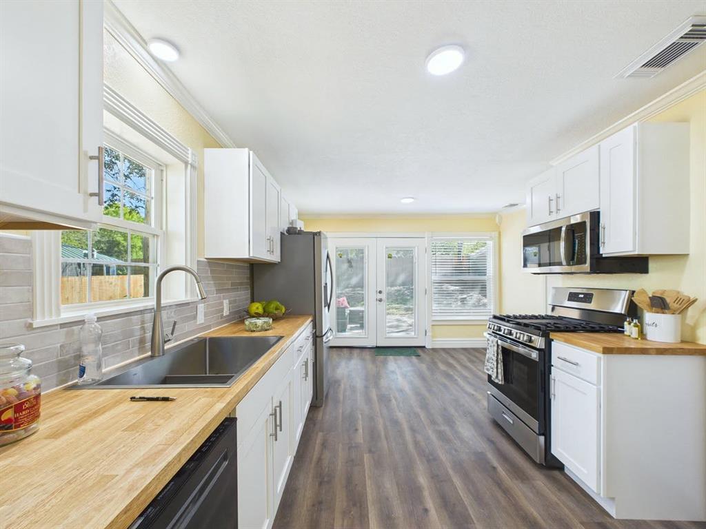 Galley kitchen featuring wood-finish countertops, white cabinetry, stainless steel appliances, and wood-finish flooring
