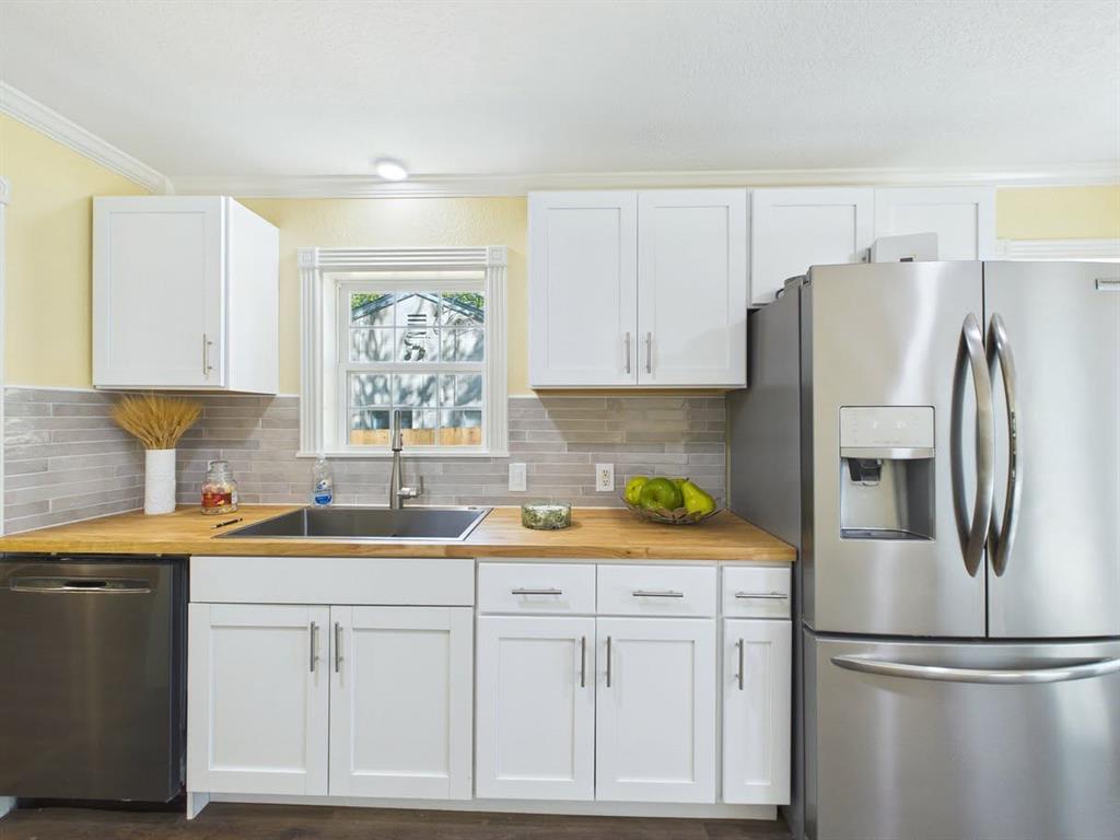 White shaker-style cabinetry with matte silver hardware, wood-finish countertops, stainless steel appliances, and a tile backsplash