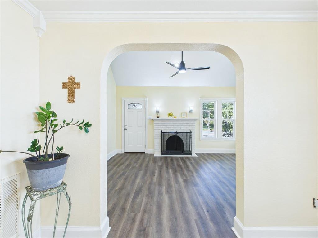 Archway entry to a living space featuring wood-finish flooring, a white brick fireplace with a black screen, a white entry door with decorative glass, and a ceiling fan