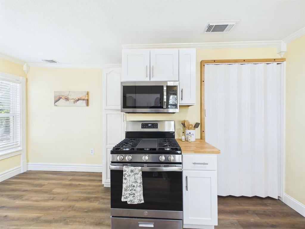 Stainless steel range with an overhead microwave, white upper and lower cabinetry, wood-finish flooring, and crown molding