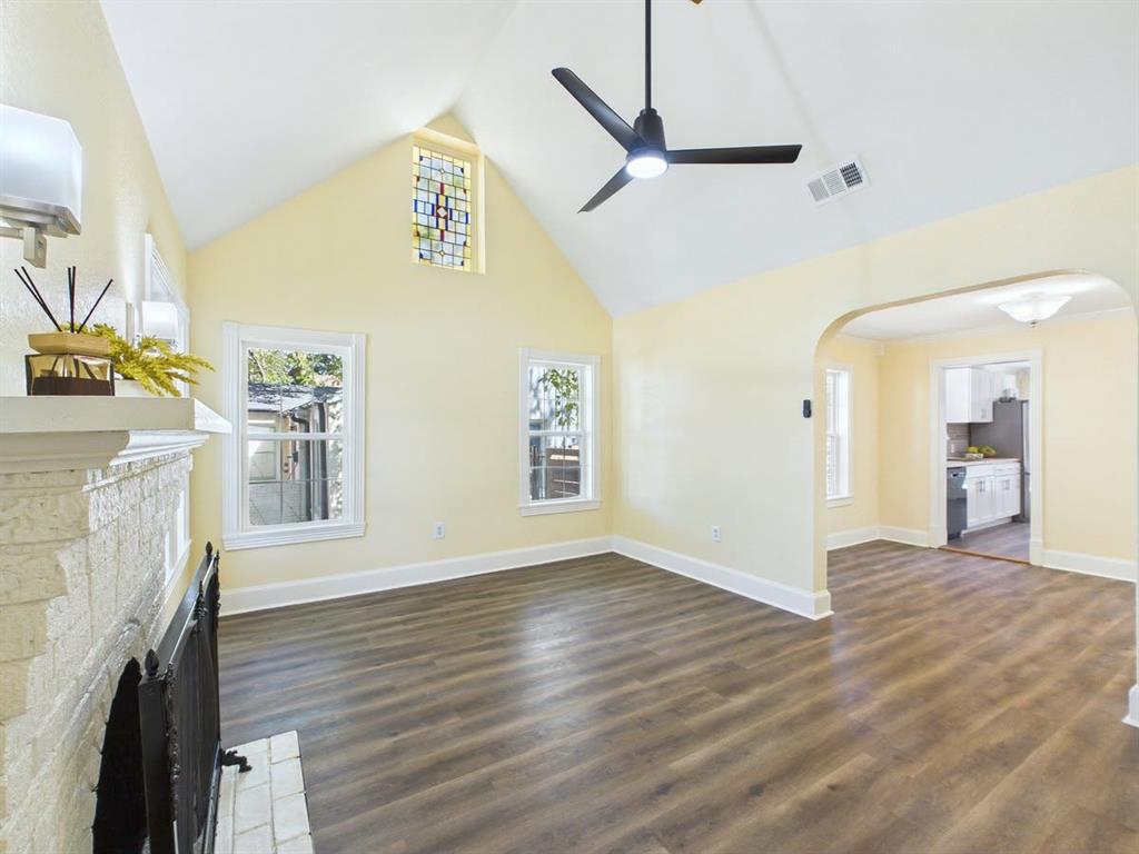 Vaulted ceiling with a stained-glass window, wood-finish flooring, a painted brick fireplace, and a modern ceiling fan