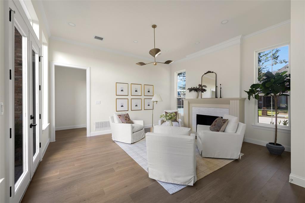 Inviting front living room with a fireplace, warm wide-plank engineered wood flooring, contemporary ceiling fixture, and large windows bringing abundant light into the space.