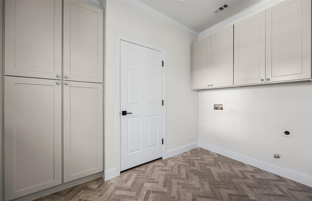 Exceptionally spacious utility room doubles as a functional mudroom, with extensive floor-to-ceiling cabinetry, additional upper storage, washer and dryer connections, and distinctive herringbone-pattern tile flooring.