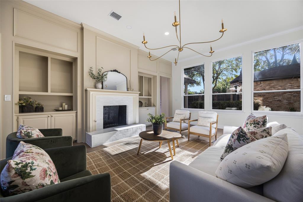 Refined living room centered around a fireplace with extensive custom built-ins and detailed millwork, complemented by a sculptural chandelier and a wall of windows overlooking the backyard.