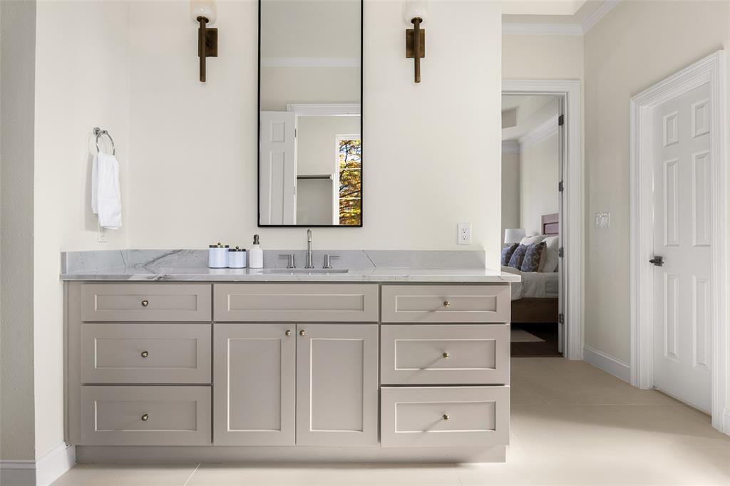 Separate primary vanity offers generous counter and storage space, tailored cabinetry, a tall framed mirror, contemporary sconces, and soft neutral finishes.