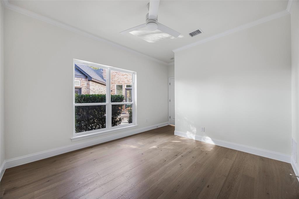 Bright secondary bedroom with warm wide-plank flooring, crown molding, ceiling fan, and an oversized window overlooking the backyard.