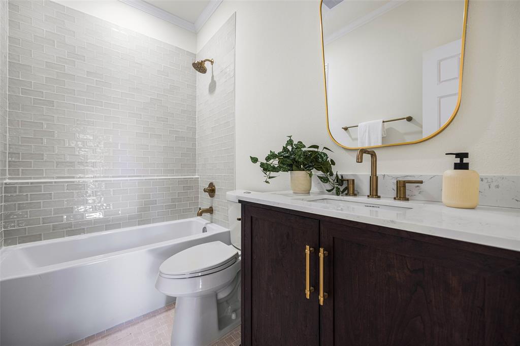 Updated full bath pairs a dark wood vanity and quartz countertop with brass-toned fixtures, a softly framed mirror, and a tub-shower combination surrounded by tile.