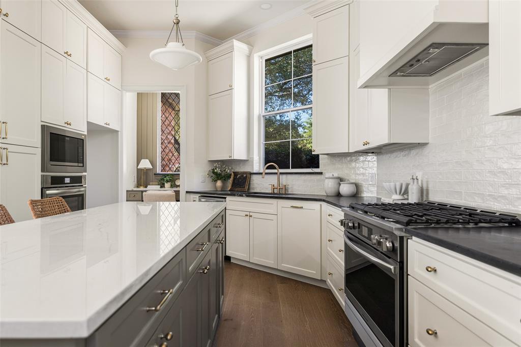 Beautifully reimagined kitchen featuring two-tone cabinetry, quartz countertops, a 6-burner gas range, custom vent hood, statement backsplash, brass-toned hardware, and an oversized center island.