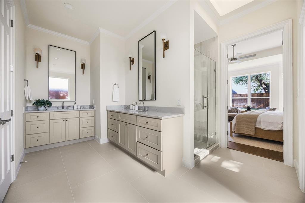 Spacious en-suite bath with separate vanities, tall framed mirrors, designer sconces, a glass-enclosed shower, abundant cabinetry, and direct connection to the primary bedroom.