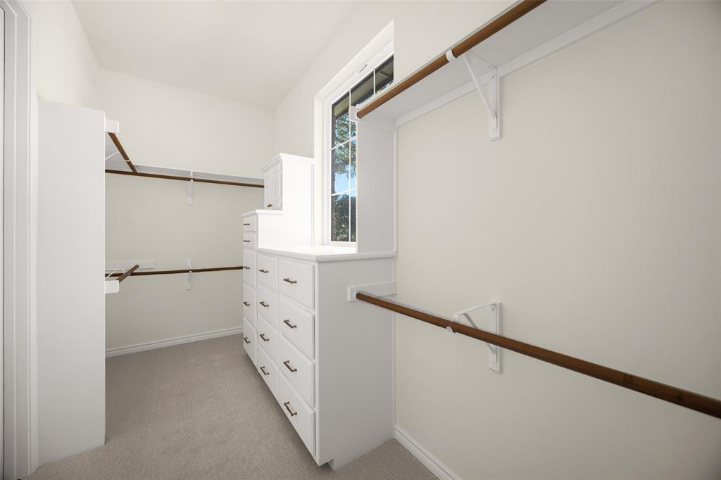 Substantial primary walk-in closet provides extensive hanging space, multiple built-in drawer banks, shelving, and a window introducing valuable natural light.