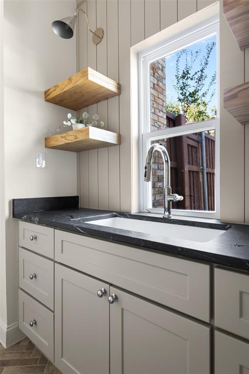 Built-in utility sink is surrounded by generous cabinetry and dark countertop space, with floating wood shelves and a large window adding both practical storage and natural light to the laundry and mudroom area.