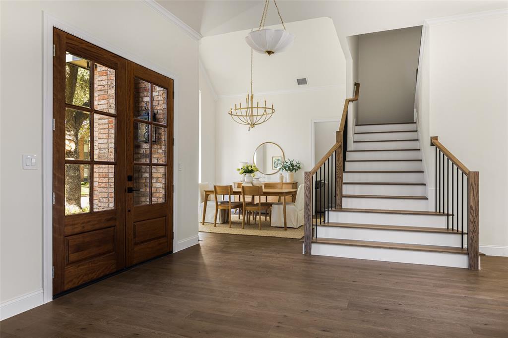 Welcoming two-story entry showcases updated double wood-and-glass doors, wide-plank flooring, a redesigned staircase with wood handrails and black iron balusters, and an open connection to the formal dining room.