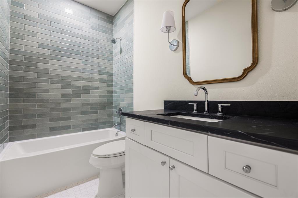Updated full bath features a tub and shower combination with floor-to-ceiling glazed tile, dark stone countertop, shaker-style cabinetry, and a decorative framed mirror.