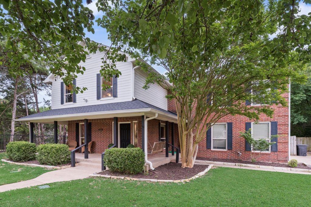 Welcoming exterior featuring a classic brick-and-siding design, mature shade trees, manicured landscaping, and a spacious covered front porch.