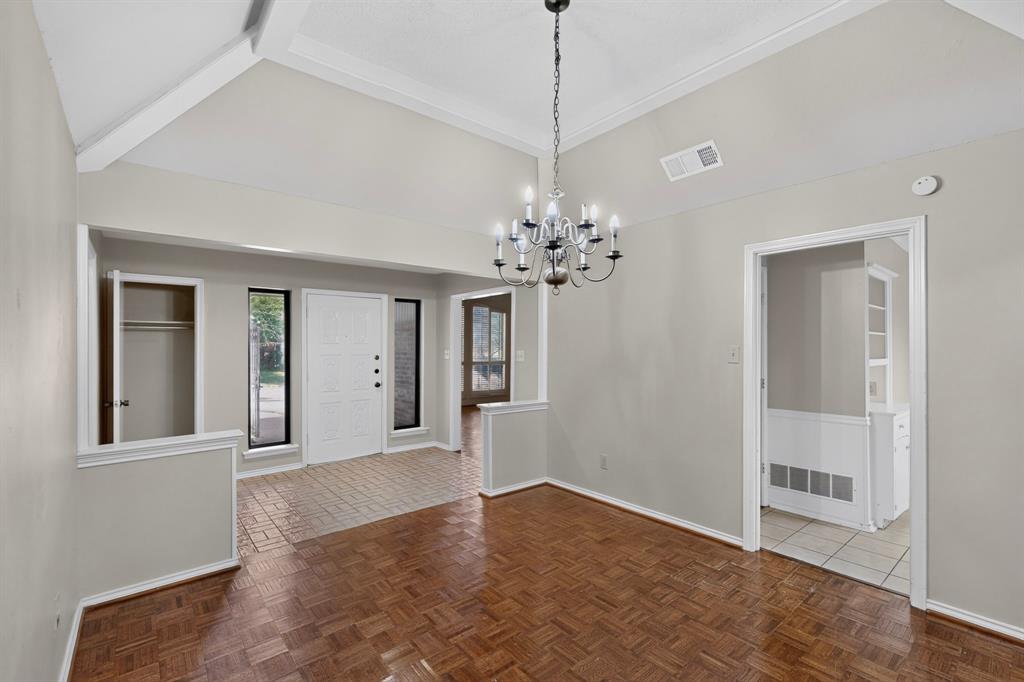 Vaulted ceiling with exposed beams, wood-finish flooring, white paneled entry door, recessed entry, and an elegant chandelier