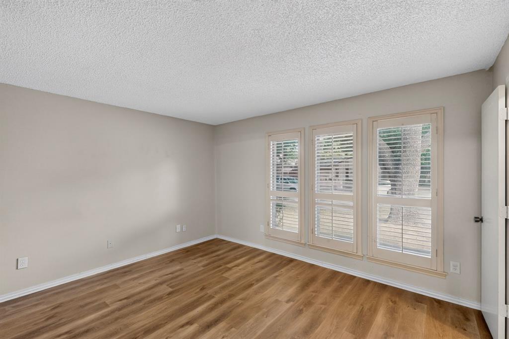 Wood-finish flooring, neutral wall paint, white trim, and three windows with plantation shutters
